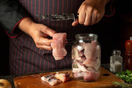 Photo for The chef prepares fresh carp fish. The cook's hand puts a fish steak into a jar for pickling. Working environment in a restaurant kitchen. - Royalty Free Image