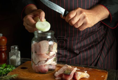 Photo for The chef is preparing a herring of fish steaks and onions on the kitchen table. Canning fish in a jar with salt and herbs. - Royalty Free Image