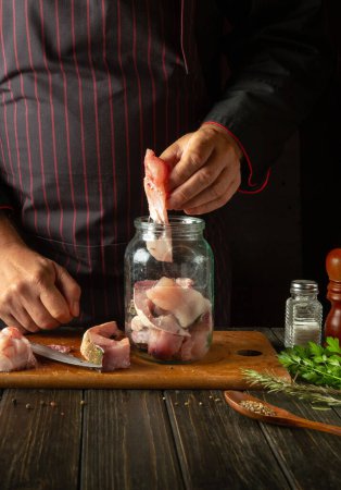 Photo for The chef prepares herring in the kitchen from fish steaks and aromatic spices. Canning fish in a jar with salt and coriander - Royalty Free Image