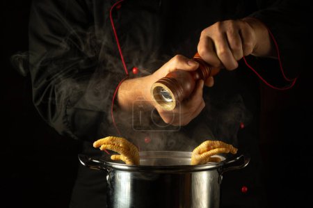 Téléchargez les photos : Le chef ajoute du poivre dans une casserole de cuisses de poulet bouillantes. Concept de préparation d'un délicieux plat d'accompagnement dans un restaurant ou une cuisine d'hôtel. - en image libre de droit