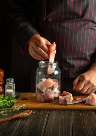 Photo for The cook prepares herring in the kitchen from fatty fish steaks and aromatic spices. The process of canning fish in a jar with salt and coriander. - Royalty Free Image