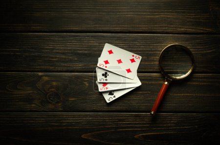 Foto de Juego de juego de póquer con cuatro de una clase o quads. Jugar a las cartas y una lupa en una mesa vintage negra en un club de póquer. - Imagen libre de derechos
