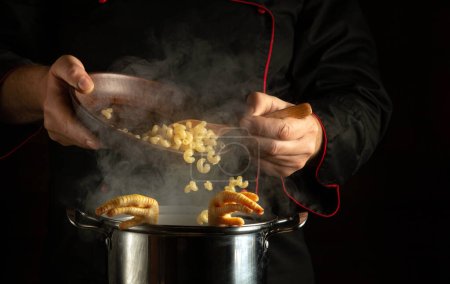Téléchargez les photos : Préparer une soupe riche. Le chef ajoute des pâtes dans une casserole de cuisses de poulet mijotantes. Espace noir pour recette ou menu. - en image libre de droit