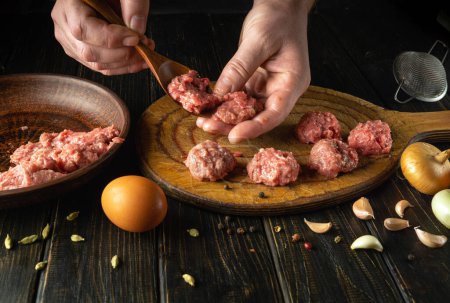 Kneading minced meat by the chef hands to prepare meatballs. Work environment with vegetables and spices on the kitchen table.
