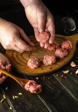 Kneading minced meat by the cook hands to prepare meatballs. Work environment with vegetables and spices on the kitchen table