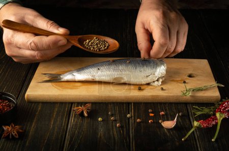 Auf dem Küchentisch bereitet der Koch Heringsfische aus der Ostsee mit Gewürzen und Koriander für ein leckeres Mittagessen zu. Arbeitsumfeld auf dem Küchentisch.