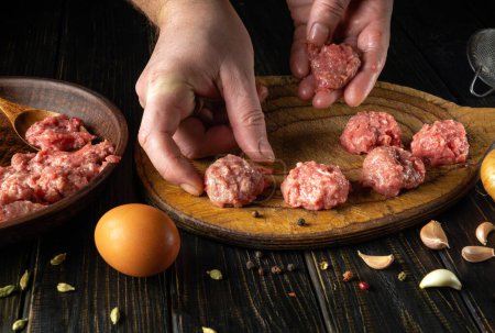 The chef hand places a meatball on the kitchen board. Preparing meat on the kitchen table for lunch. Cooking recipes and nutrition concept.