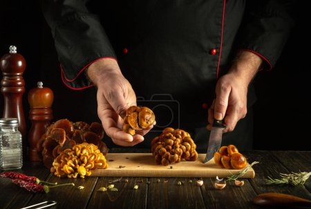 A knife in the hand of a chef for preparing mushrooms in the saloon kitchen. Low key concept of cooking mushroom dish for lunch.