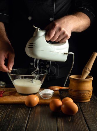Ein Stabmixer in der Hand eines Küchenchefs zur Zubereitung eines Omeletts mit Milch und Eiern. Low-Key-Konzept der Zubereitung eines Milchgerichts zum Frühstück.