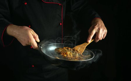 Gebratenen Fisch in einer Pfanne in den Händen eines Küchenchefs zubereiten. Konzept des Zubereitungsprozesses eines Fischgerichtes mit wenig Platz für Werbung.
