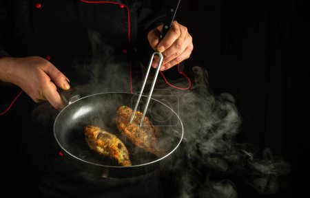 Der Koch brät Flussfisch in einer heißen Pfanne in der Kneipenküche. Eine schlichte Idee zur Zubereitung einer köstlichen Fischkost. Schwarzer Raum für Werbung.