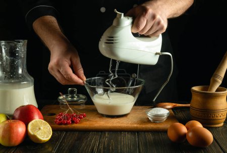 Ein professioneller Koch bereitet mit einem elektrischen Handmixer ein Eieromelett mit Milch zu. Low-Key-Konzept der Zubereitung von leckerem Frühstück in Salonküche.