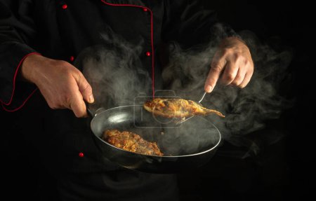 Der Koch brät Fisch in einer Pfanne. Low-Key-Konzept der Zubereitung eines köstlichen Fischgerichts zum Mittagessen.
