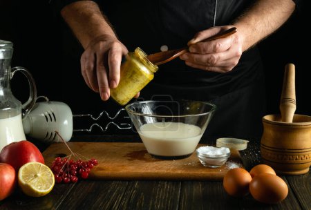 Ein professioneller Koch fügt einem Milchshake auf dem Küchentisch Honig hinzu. Low-Key-Konzept der Zubereitung eines köstlichen Abendessens mit Eiern und Milch in der Küche.