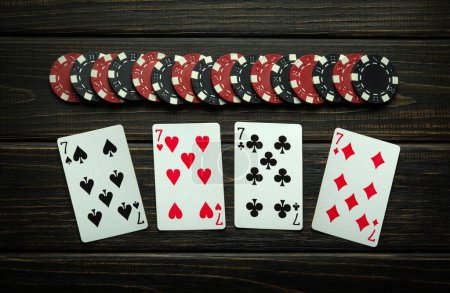 Photo for Playing cards in the game of poker with chips from winning on a vintage table in a clubhouse. Lucky win concept with four of a kind or quads combination in low key. - Royalty Free Image