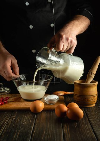 Ein professioneller Koch bereitet in der Küche mit einem elektrischen Handmixer einen Milchshake mit Früchten zu. Der Koch gießt Milch in einen tiefen Glasteller. Ein Menü mit köstlichen Rezepten für ein schlichtes Restaurant.