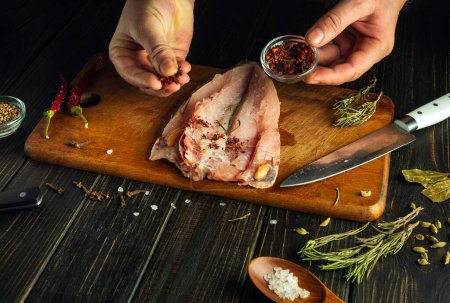 Añadir especias aromáticas secas a los filetes de pescado fresco de las manos del chef. Plato nacional de pescado, hecho en casa según una receta única.