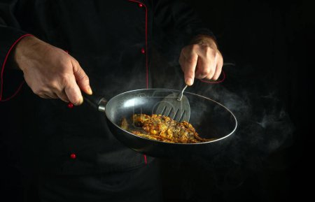 Der Koch brät Karauschen in einer heißen Pfanne. Unauffälliges Konzept der Zubereitung eines Fischgerichts zum Frühstück. Schwarzer Raum für Menü oder Rezept.