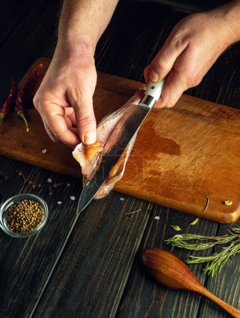 Der Koch schneidet oder putzt Fisch mit einem Messer auf dem Küchentisch. Low-Key-Konzept des Kochens Fischgericht auf dem Küchentisch im Restaurant