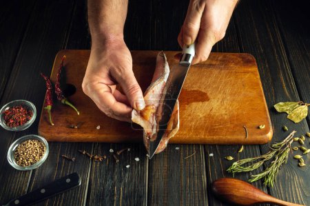 Das Kochen von Meeresfischen durch die Hände eines Kochs. Chef Hände schneiden einen Fischkadaver auf einem Küchentisch.