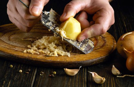 Zugeschnittenes Bild eines Kochs, der rohe Kartoffeln mit einer Reibe reibt, um Chips zuzubereiten. Kulinarisch gesundes pflanzliches Ernährungskonzept.