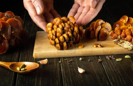Close-up of a chef hands sorting raw fresh Flammulina velutipes or velvet shank mushrooms on a kitchen board before preparing a diet dinner.