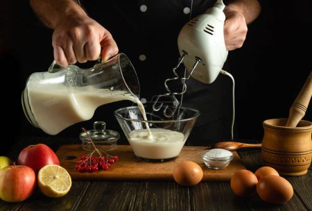 El chef prepara un cóctel de leche y frutas con una batidora eléctrica de mano. Concepto bajo llave de preparar una bebida refrescante con las manos de un cocinero en la cocina de una casa pública.