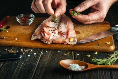 El cocinero añade romero aromático a los filetes de pescado fresco con las manos. Un concepto bajo en clave para la preparación de un plato nacional de pescado de acuerdo con una antigua receta única.