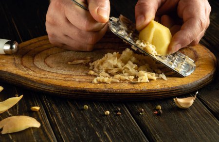 Rohe Kartoffeln mit der Reibe in den Händen eines Kochs reiben. Vorbereitung eines Gemüsemenüs für ein vegetarisches Abendessen.