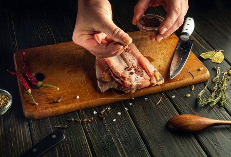 Die Hände des Küchenchefs fügen den frisch geschnittenen Fischfilets aromatische Gewürze hinzu. Eine zurückhaltende Idee, um ein nationales Fischgericht nach einem einzigartigen Rezept zuzubereiten.