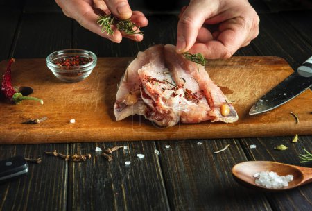 Le cuisinier prépare un plat de poisson avec ses mains sur la table de cuisine. Ajouter du romarin pour la saveur de couper la carcasse de poisson.