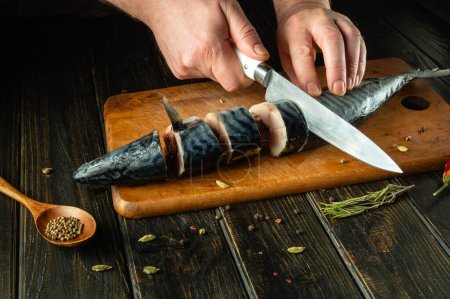 Un chef de pescado prepara caballa fresca en la cocina. Scomber debe cortarse en trozos pequeños antes de hornear. Espacio publicitario.