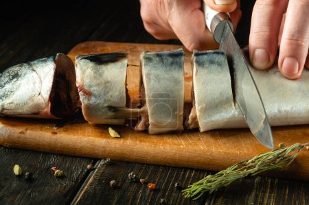 Großaufnahme eines Kochs, der vor dem Braten Makrelenfische mit einem Messer schneidet. Das Konzept der Zubereitung eines Fischmenüs zum Mittagessen mit Gewürzen.