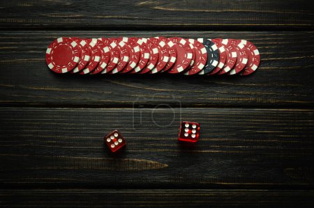 Red winning chips and dice with a winning combination of two sixes on a vintage dark casino table. Low key concept of fortune or luck in a poker club.