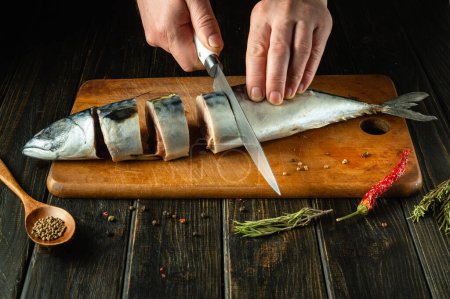 A chef cuts sea fish with a knife before grilling. Spices on the kitchen table for preparing a delicious lunch with mackerel.