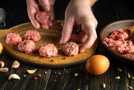 Cooking meatballs by the hands of a chef with minced meat on a kitchen board. Low key concept of cooking dinner on the kitchen table.