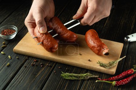 Preparing to cook a delicious grill with Munich sausages. A fork with sausages in the hands of a man on the kitchen table. Place for recipe.