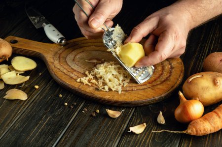 Ein Koch reibt Kartoffeln, um ein gesundes Frühstücksgericht zuzubereiten. Low-Key-Idee, zu Hause frisches Gemüse auf dem Küchentisch zu kochen.