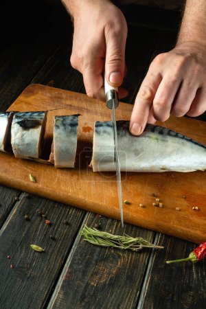 The chef cuts raw mackerel fish on a cutting board before preparing the dish. Low key concept for cooking fish menu. European cuisine.