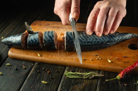 Roher Fisch wird mit einem Messer in der Hand eines Kochs zum Salzen mit Gewürzen geschnitten. Das Konzept, Hering mit Fisch auf dem Küchentisch zuzubereiten