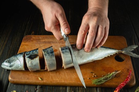 Die Hände des Küchenchefs schneiden Makrelen mit einem Messer in Stücke, bevor sie sie zum Mittagessen braten. Arbeitsumfeld in der Küche eines öffentlichen Hauses.