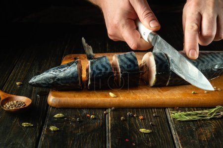 El chef corta un pescado Scomber con un cuchillo en una tabla de cortar la cocina. Menú o receta para restaurante u hotel. Cocinar las manos cerca. Espacio publicitario.