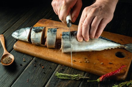 The cook cuts raw mackerel fish on a cutting board before preparing the dish. Low key concept for cooking fish menu. Advertising space.