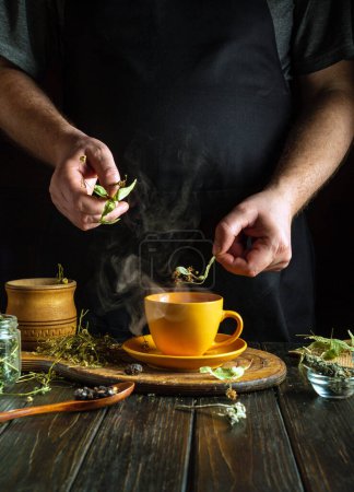 Tea made from dried linden and chamomile flowers for colds in the hands of a man on the kitchen table. Traditional medicine concept made from beneficial and medicinal herbs.