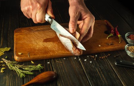 Die Hände des Kochs schneiden mit einem Messer gefrorenen Seehecht auf einem hölzernen Schneidebrett. Nationales Fischgericht, zubereitet in einem Restaurant nach einem einzigartigen Rezept.