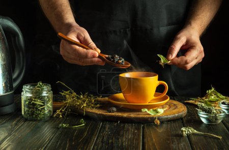 Der Koch brüht gesunden Tee aus trockenen Heilkräutern. Eine Hand hält einen Löffel mit trockenen Hagebutten, die in eine gelbe Tasse gegeben werden müssen. Schwaches Konzept der traditionellen Medizin.