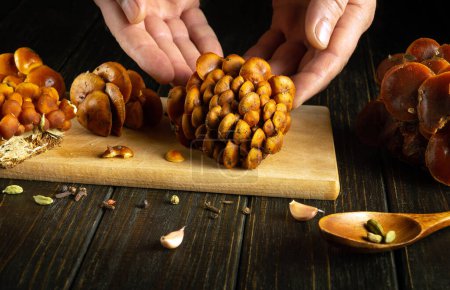 Hände eines Kochs sortieren rohe frische Flammulina velutipes Pilze oder Samtschulterpilze auf einem Küchentisch, bevor sie ein Diätfrühstück zubereiten.