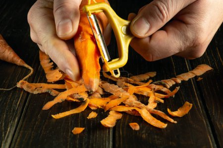 Peeling carrots for preparing a vegetable diet dish. Close-up of a chef hands with a vegetable peeler while working.