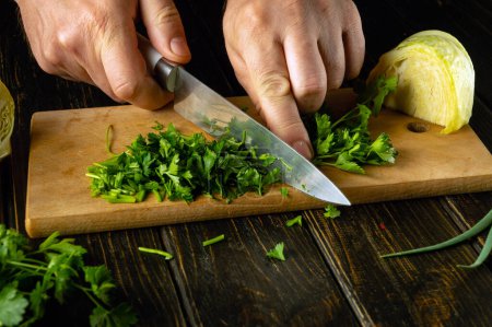 The chef chops fresh parsley with a knife on a wooden cutting board. Vegetarian menu for a restaurant or hotel.