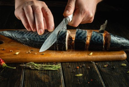 Cortar pescado en una tabla de la cocina. Las manos del chef usan un cuchillo para cortar caballa para preparar un plato de pescado para el almuerzo..